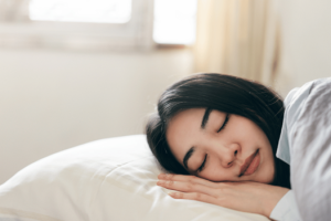 Young woman sleeping peacefully in bed, highlighting the importance of proper sleep for women’s health and well-being.